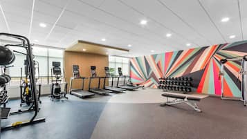 A gym with treadmills, weight machines, and a colorful wall.