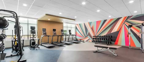 A gym with treadmills, weight machines, and a colorful wall.