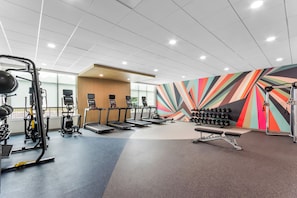 A gym with treadmills, weight machines, and a colorful wall.