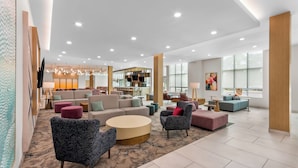 A spacious lobby with seating areas, a kitchen in the background, and large windows.
