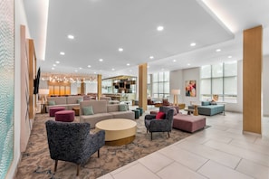 A spacious lobby with seating areas, a kitchen in the background, and large windows.