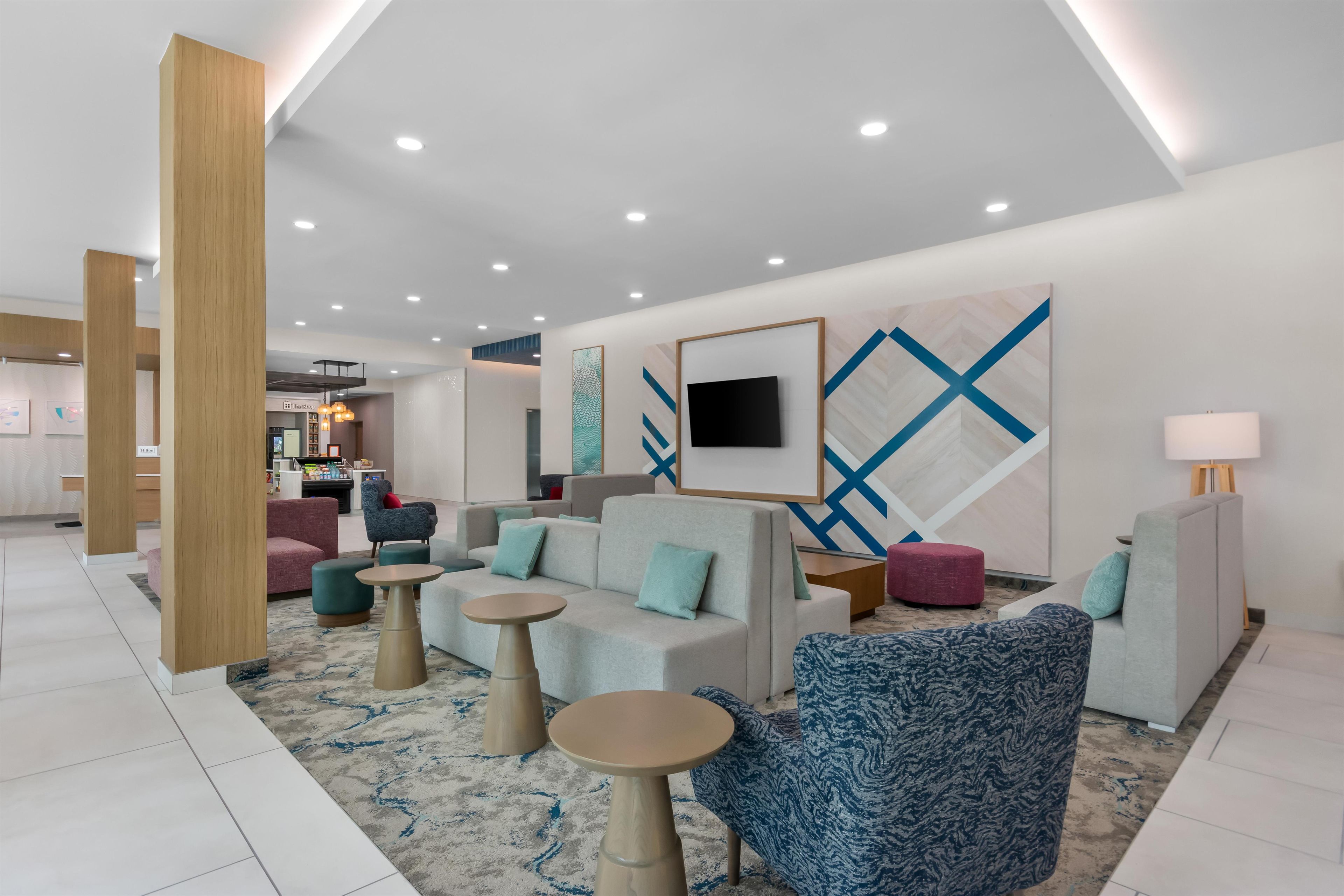 A modern hotel lobby with seating areas, a flat-screen TV, and artwork on the walls.
