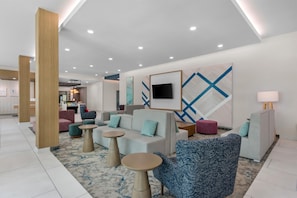 A modern hotel lobby with seating areas, a flat-screen TV, and artwork on the walls. - Hilton Garden Inn Destin Commons (Destin)