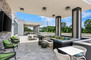 An outdoor patio area with seating arrangements, a flat-screen TV, and a view of the parking lot. - Hilton Garden Inn Destin Commons (Destin)