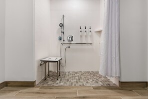 Zona de ducha con suelo de baldosas, ducha con cabezal, ducha de mano y estante con artículos de aseo.