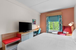 Habitación de hotel con cama, escritorio, televisor de pantalla plana, silla, mesita y ventana con cortinas.