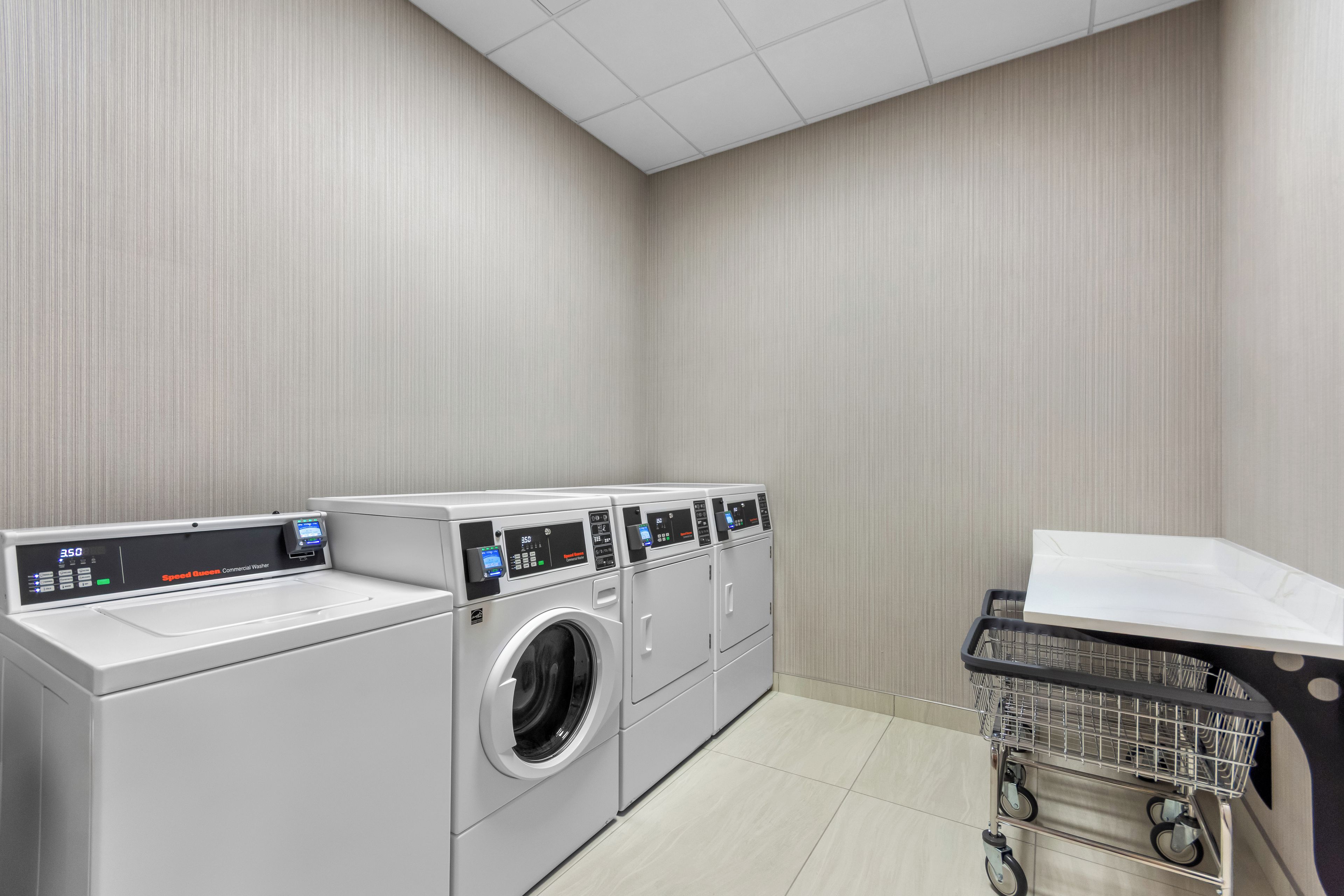 A laundry room with multiple washing machines and a cart with a white item on it.