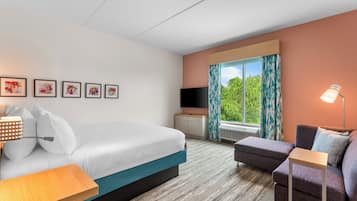A hotel room with a bed, a desk, a chair, a TV, and a window with curtains.