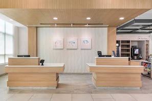 A reception area with two wooden reception desks, a patterned wall, and a vending machine in the background.