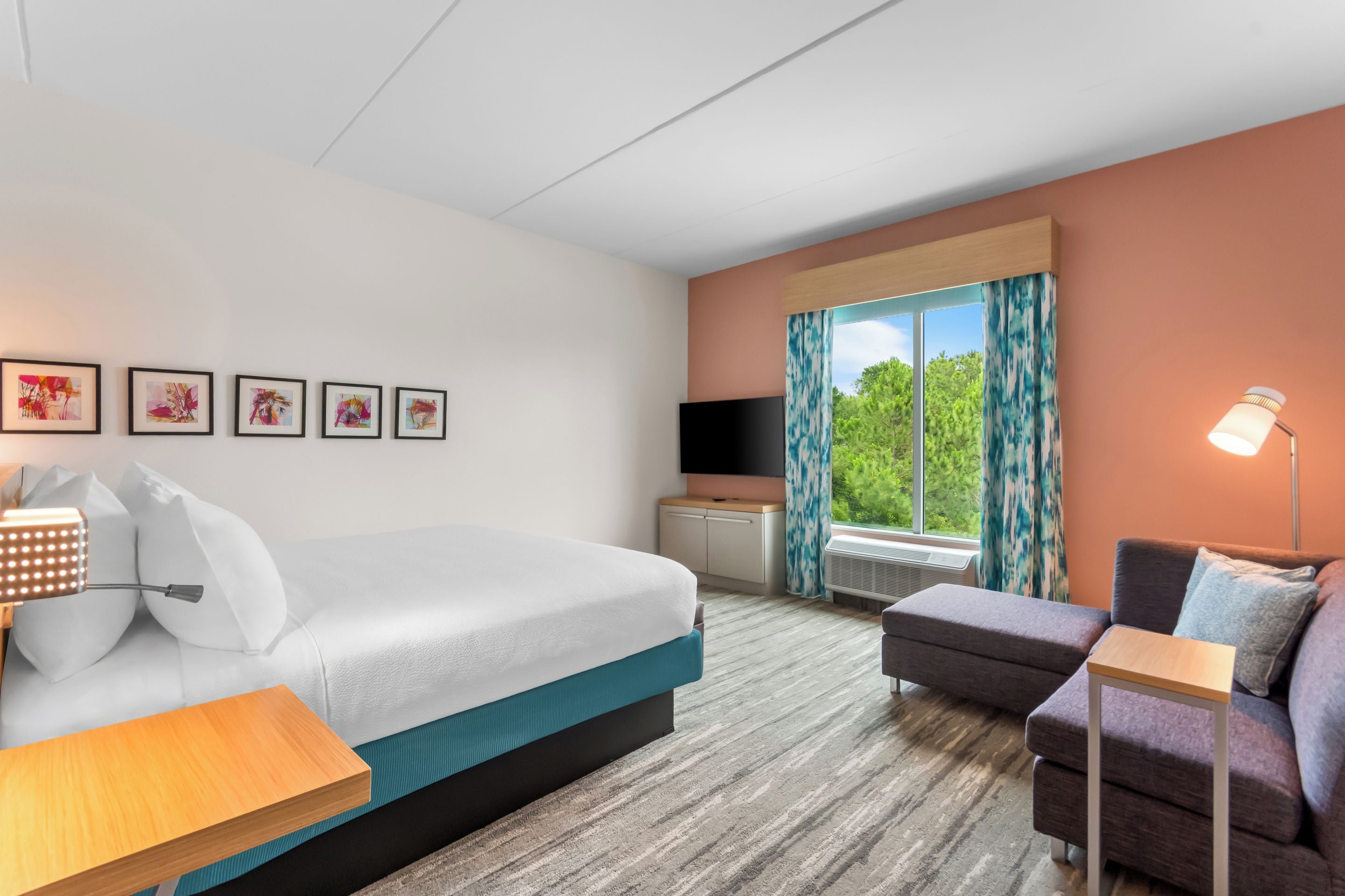 A hotel room with a bed, a desk, a chair, a TV, and a window with curtains.