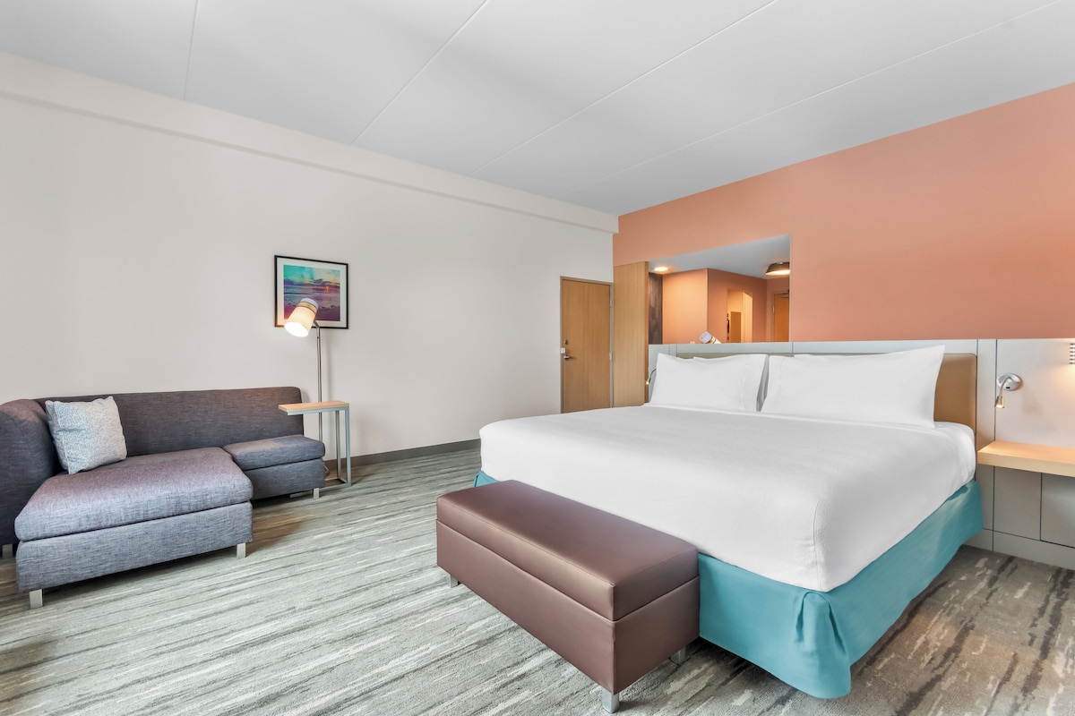 A hotel room with a bed, a sofa, a small table, and a nightstand.
