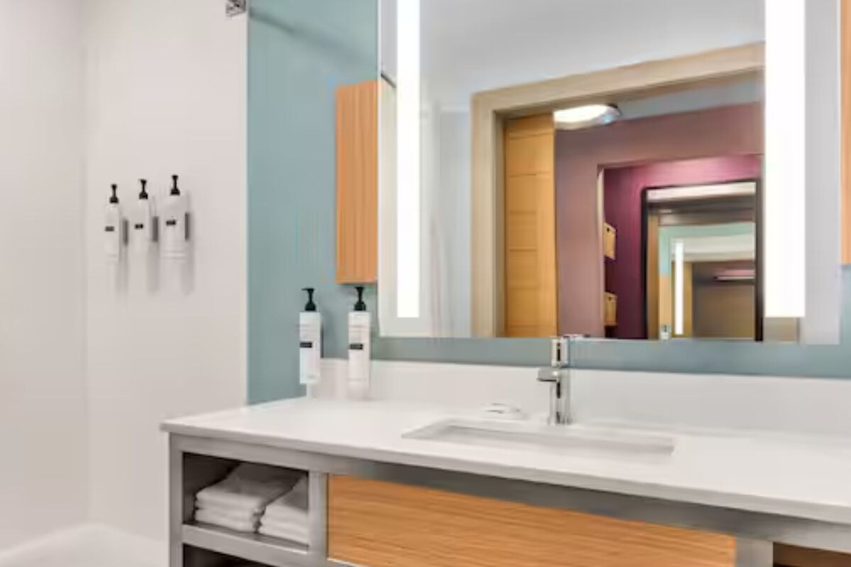 Un baño con un lavamanos blanco, un espejo y dos botellas de artículos de tocador en la pared.