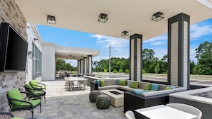 An outdoor patio area with seating arrangements, a flat-screen TV mounted on the wall, and a view of the surrounding greenery.