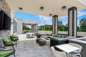 An outdoor patio area with seating arrangements, a flat-screen TV mounted on the wall, and a view of the surrounding greenery.