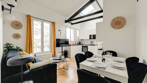A modern living room with a sofa, a dining table set for two, and a kitchen in the background. - Spacious Appartement 2BR/7P - Nogent-sur-Marne (Nogent-sur-Marne)