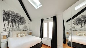 Een slaapkamer met een groot bed, dakraam, een raam met gordijnen, een spiegel en een muurschildering.