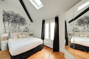 Ein Schlafzimmer mit einem großen Bett, einem Oberlicht, einem Fenster mit Vorhängen, einem Spiegel und einem Wandbild.