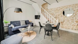 Een moderne woonkamer met een bank, salontafel en stoelen, een trap met een stenen muur, en een eethoek met een tafel en stoelen.
