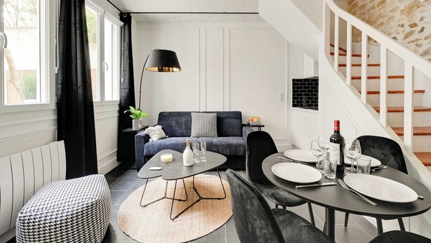 Een moderne woonkamer met een bank, salontafel, eettafel en een trap met een stenen muur.