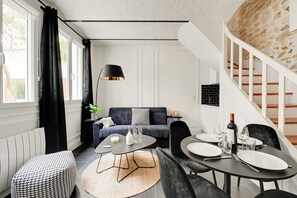 Ein modernes Wohnzimmer mit Sofa, Couchtisch, Esstisch und einer Treppe an einer Steinwand.