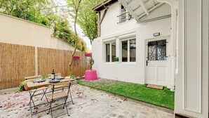 Een terras met een eettafel, een houten omheining en een wit gebouw met een deur en raam.