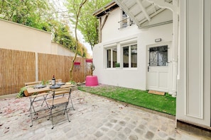 Eine Terrasse mit Esstisch, ein Holzzaun und ein weißes Gebäude mit Tür und Fenster.
