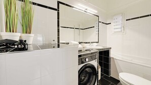 Een badkamer met een wasmachine, een wastafel, een toilet en een spiegel.