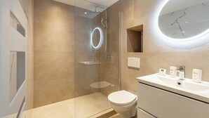 Une salle de bain moderne avec une douche à parois de verre, un lavabo blanc agrémenté d’articles de toilette et un grand miroir.