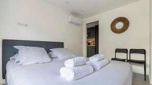 Un lit bien fait, avec du linge de lit et des serviettes blanches, une tête de lit sombre et un miroir fixé au mur.