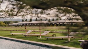 A poolside area with lounge chairs and umbrellas, surrounded by greenery and a view of the landscape. - Luxury Provençal house – Pool, nature & spa (Villes-sur-Auzon)