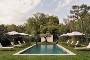 Ein Pool mit Liegestühlen und Sonnenschirmen, umgeben von viel Grün.