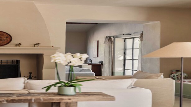 A living room with a sofa, a table with a vase of flowers, a fireplace, and a view through an open door. - Luxury Provençal house – Pool, nature & spa (Villes-sur-Auzon)