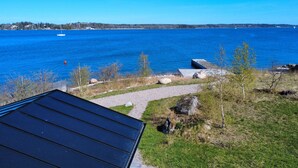 Udsigt over kysten med klart himmel, et vandareal og en sti, der fører hen til en bygning med mørkt tag.