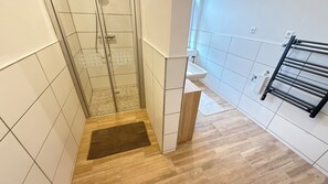 A bathroom with a shower, a sink, a towel rack, and a wooden cabinet. - Apartments Zum Weihnachtsland "Anton Günther" (Stützengrün)