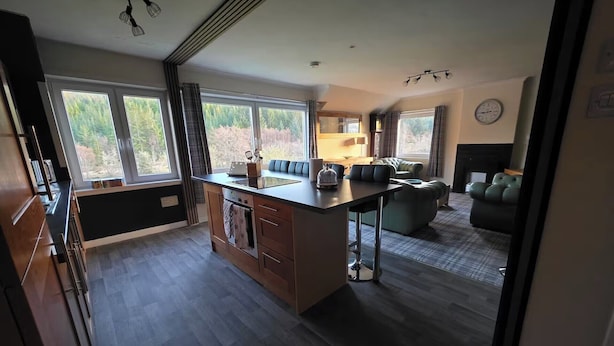 Eine moderne Küche mit einer zentralen Kochinsel, großen Fenstern und einer gemütlichen Sitzecke mit Sofa und Hocker.