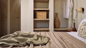 Ein Schlafzimmer mit einem Bett, einem Kleiderschrank, einer eingebauten Regalverkleidung mit Körben, einem Kleiderständer und einer Vase.