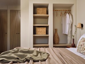 Un dormitorio con una cama, un armario, una estantería con cestas, un perchero con ropa y un florero.