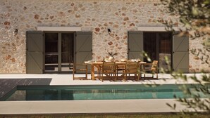 Ein Haus mit Steinverkleidung, einem Ziegeldach und einem Poolbereich mit Gartenmöbeln.