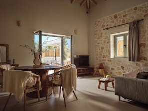 A spacious living area with a round wooden table, wicker chairs, a sofa, a television, and a stone wall. - Conte Maris IV - The True Mediterranean Escape! (Zakynthos)