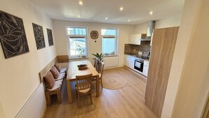 A compact kitchen with a dining area, wooden flooring, and a clock on the wall.