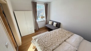 Une chambre à coucher comprenant un lit, un canapé, une armoire, une fenêtre avec des rideaux et une vue sur l’extérieur.