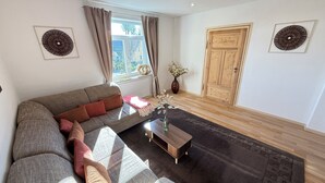 A living room with a sofa, a coffee table, a vase with flowers, a wooden door, and two wall decorations.