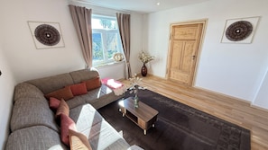 A living room with a sofa, a coffee table, a vase with flowers, a wooden door, and two wall decorations. - Holiday apartment Zum Weihnachtsland " Karl Stülpner" (Stützengrün)