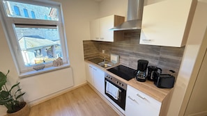 A compact kitchen with a window, a stove, a sink, and a coffee maker. - Holiday apartment Zum Weihnachtsland " Karl Stülpner" (Stützengrün)