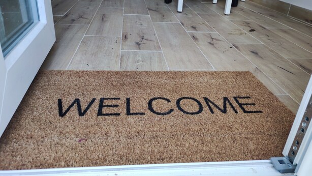 A welcome mat with 'WELCOME' written on it, a wooden floor, and white chairs in the background. - 50 special apartment (Pontedera)