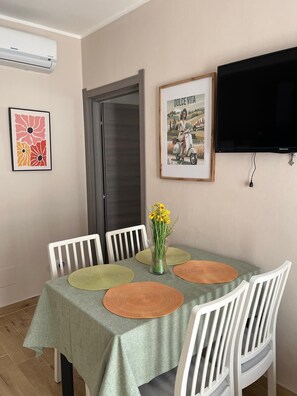 A dining area with a table set for four, surrounded by white chairs, a framed picture, and a mounted television. - 50 special apartment (Pontedera)