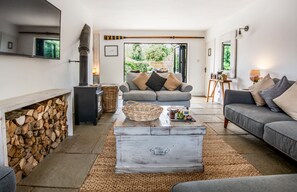 Ein Wohnzimmer mit Kamin, einer Couch, einem Couchtisch und Blick durch eine geöffnete Tür.