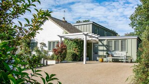 Ein Haus mit weißer Fassade, einer überdachten Terrasse und einem kleinen Garten.