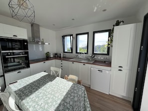 A modern kitchen with a Bosch oven, a dining table with a patterned tablecloth, and a view through the windows. - Quiet family house between sea and mountains with swimming pool - sleeps 8 (Bassussarry)
