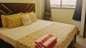 Ein Hotelzimmer mit Bett, Fenster mit Blick, Deckenleuchte und einem Bild an der Wand.